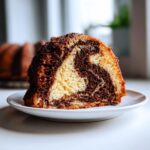Close-up of a thick slice of german marble cake showing distinct vanilla and chocolate swirls on a white plate.