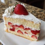 A perfect slice of japanese strawberry shortcake featuring light sponge cake, whipped cream, and sliced strawberries.
