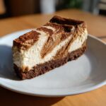 A close-up of a rich slice of biscoff cheesecake showing a marbled swirl pattern on top of a dark crumb crust.