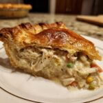 Close-up of a generous slice of chicken pot pie showing creamy filling, shredded chicken, peas, and corn under a flaky golden crust.