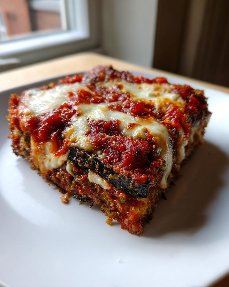 A close-up serving of baked eggplant parmesan, layered with sauce and melted mozzarella cheese.