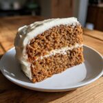 A moist slice of spice cake with thick cream cheese frosting on a white plate.