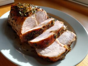 A sliced crockpot pork tenderloin, seasoned with herbs, resting on a light blue plate in sunlight.