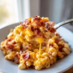 A spoonful of creamy, cheesy slow cooker cheddar corn with bacon being lifted from a bowl.