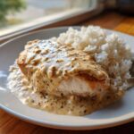 A close-up of perfectly cooked smothered chicken and rice, featuring a creamy, herb-flecked sauce over the chicken breast.