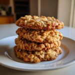 A tempting stack of four soft oatmeal cookie treats piled high on a white plate.