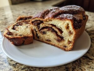 A loaf of soft raisin bread, dusted with powdered sugar, with one slice cut and resting next to it on a white plate.