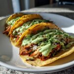 Close-up of three delicious southwest chicken tacos topped with creamy green sauce and cilantro.