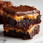 Two stacked squares of decadent millionaire brownies showing the rich chocolate base, gooey caramel layer, and chocolate topping.