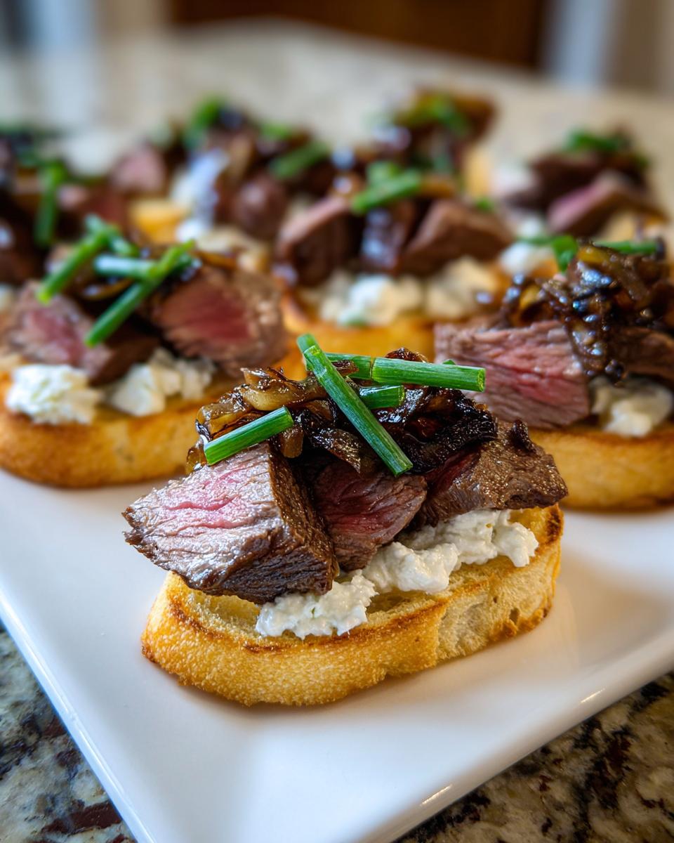 Close-up of steak crostini topped with creamy cheese, caramelized onions, and chives, showing medium-rare steak.