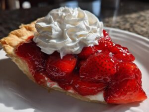 Close-up of a slice of strawberry pie showing glossy, whole strawberries, a creamy layer, and a dollop of whipped cream.