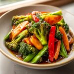 Close-up of a colorful teriyaki vegetable stir fry featuring broccoli, carrots, red peppers, and snap peas coated in sauce.