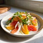 A bright, colorful citrus salad featuring segments of orange and grapefruit, shaved fennel, and topped with fresh arugula.