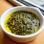 Close-up of a white bowl filled with vibrant green herbs, spices, and olive oil, perfect for an olive oil bread dip.