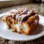 A close-up of a single, gooey Apple pie cinnamon rolls slice topped with white icing.