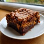 A close-up of a fudgy butterscotch brownies square with a crackly top, served on a white plate.