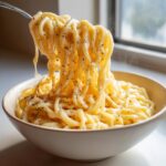 A fork lifts creamy, cheesy noodles seasoned with black pepper from a bowl of Carbonara buldak ramen.