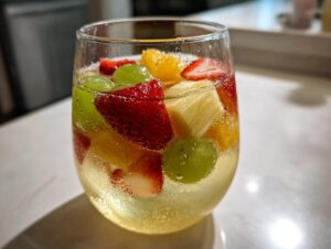 Close-up of a glass filled with bubbly Moscato sangria, loaded with strawberries, green grapes, pineapple, and orange slices.