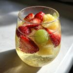 Close-up of a glass filled with bubbly Moscato sangria, loaded with sliced strawberries, pineapple chunks, and a green grape.