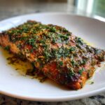 Close-up of a perfectly cooked Greek salmon fillet generously topped with fresh dill and lemon zest, resting in its juices.