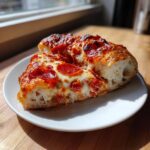 Two thick slices of homemade pepperoni pizza showing bubbly cheese and a fluffy crust, served on a white plate.