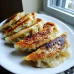 Five golden-brown, pan-fried cabbage dumplings arranged in a row on a white plate.