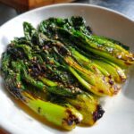 Close-up of vibrant, glossy sautéed bok choy topped with toasted sesame seeds and chili flakes.