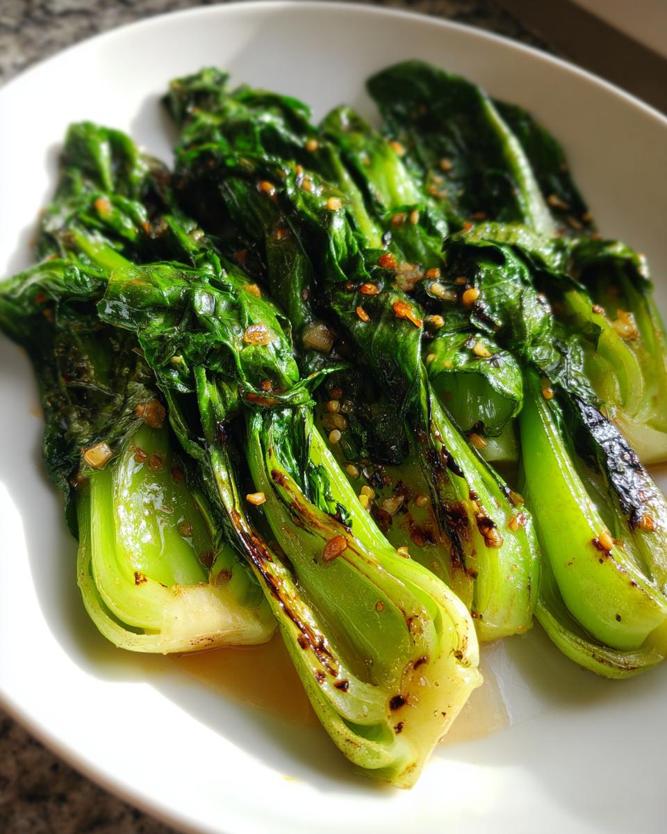 Close-up of vibrant green sautéed bok choy halves glistening with sauce and topped with minced garlic.