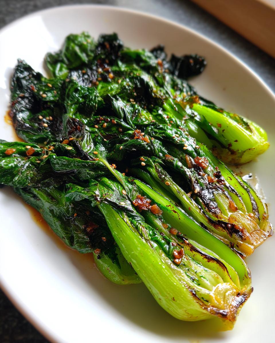 Close-up of vibrant green sautéed bok choy halves topped with sesame seeds and a savory sauce.