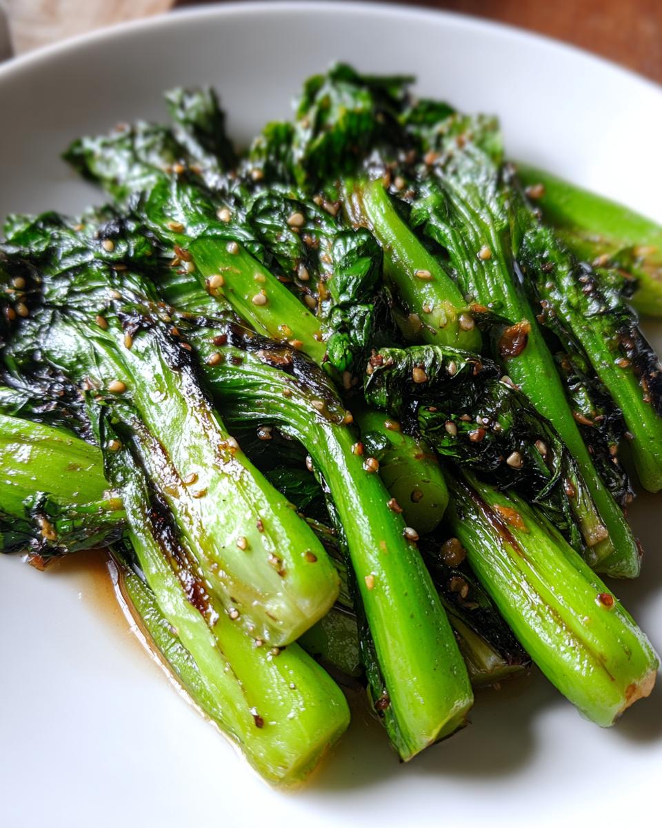 A close-up image of vibrant green sautéed bok choy coated in a savory sauce and sprinkled with toasted sesame seeds.