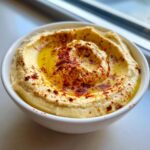 A close-up of a bowl of silky Traditional hummus, swirled and topped with a generous drizzle of olive oil and paprika.