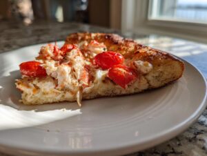 A close-up slice of lobster pizza topped with generous chunks of white lobster meat and bright red roasted cherry tomatoes.