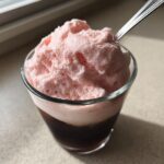 Close-up of a glass topped with thick, fluffy pink strawberry cold foam and a spoon.