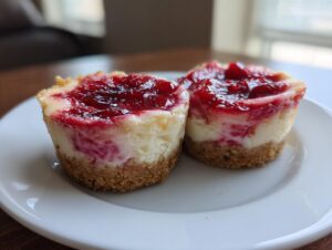 Two perfectly baked Strawberry Rhubarb Mini Cheesecakes with graham cracker crusts and bright red topping.